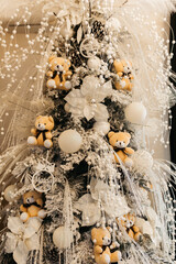 A Christmas Tree With Ornaments And Teddy Bears As Decoration. The tree is large, it is decorated with lights, tinsel, and other ornaments. 
