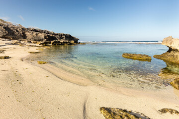 Plage au bord d'un lagon calme &eacute;meraude et turquoise prot&eacute;g&eacute; par une barri&egrave;re de corail et encadr&eacute;e de rochers