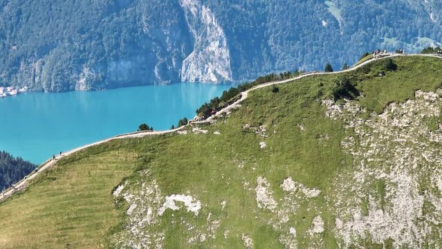 Hiker hikers on a mountain ridge trail in Switzerland, swiss alps mountains. Recreational summer leisure activity. Green alps and grass. Aerial drone overhead.