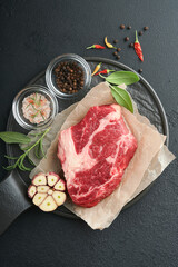 Raw beef steak. Raw fresh Chuck roll steak with rosemary, salt and pepper on cutting board on dark concrete background. Raw beef steak and spices for cooking.