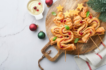 Christmas or New Year appetizer. Christmas tree shape puff pastry buns with cheese and ham. Group of Christmas tree shapes on wooden board. Festive idea for Christmas or New Year dinner. Top view.