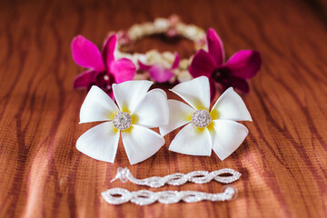 Fototapeta na wymiar Frangipani flower with diamond earrings decorated inside, beautiful and outstanding, with orchids and a necklace behind the garland in the picture laying on brown cloth.