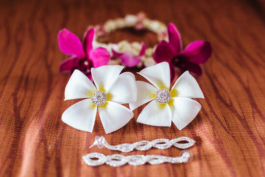 Frangipani flower with diamond earrings decorated inside, beautiful and outstanding, with orchids and a necklace behind the garland in the picture laying on brown cloth.