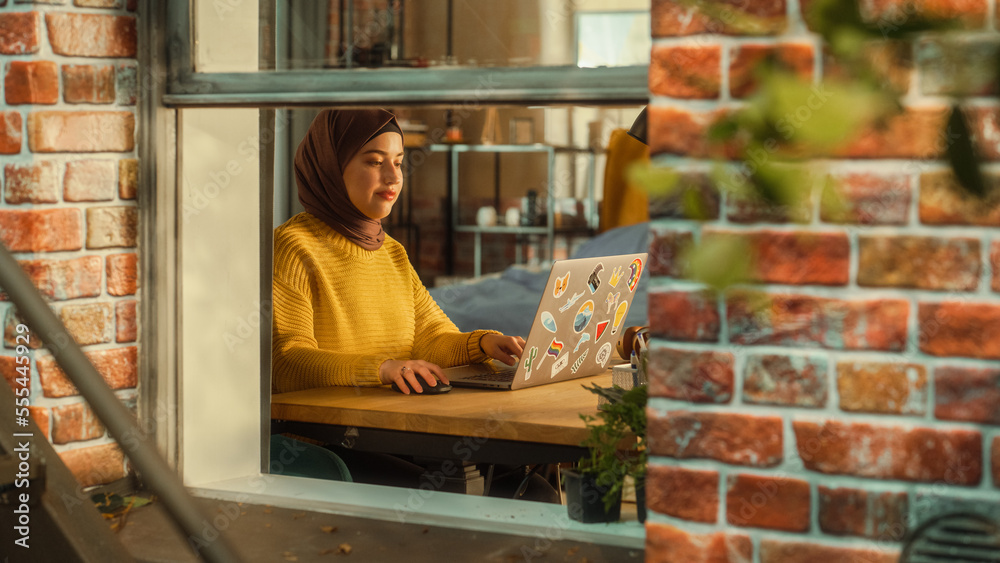 Poster Smiling Arab Woman Using Laptop Computer in Her Apartment on a Warm Sunny Day. Remote Work Concept with Freelancer or Business Manager Working From Home. Outside the Window Shot.