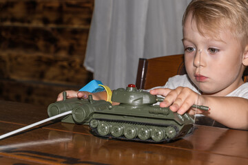 A little boy European German age 3 years old plays war with a tank model in a dark room on the table