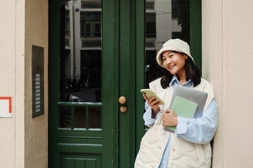 Smiling asian girl using smartphone while standing outdoors