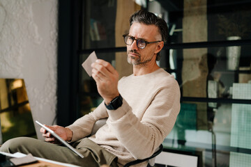 Mature grey man examining samples while working with tablet computer