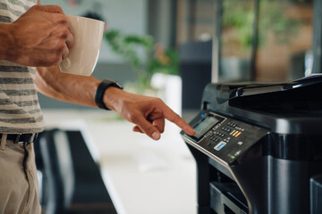 Young man drinking coffee and using copy machine in office