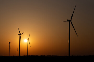 Silhouettes of wind turbines against the setting sun.