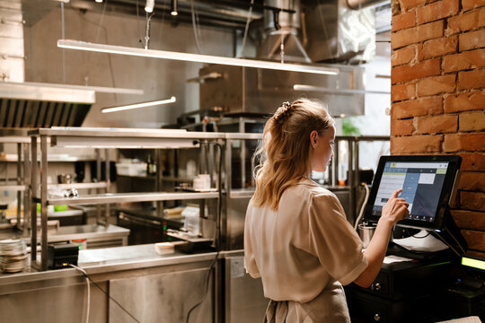 Young woman waitress using computer terminal while working in restaurant