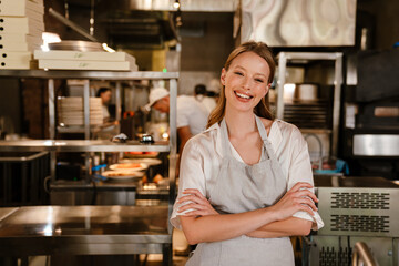 Cheerful woman chef cook standing in kitchen of a restaurant with arms folded