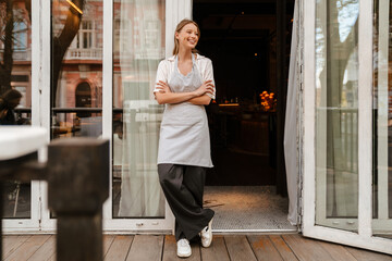 Young woman smiling while standing outdoors near restaurant with arms folded