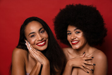Two smiling half-naked women posing isolated over red background