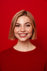Smiling blonde woman posing isolated over red studio background