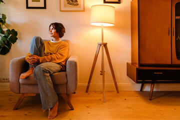 Young woman sitting in armchair while resting at home