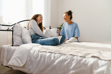 Young women laughing and chatting together while sitting in bed at home