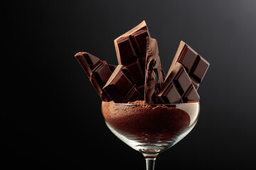 Broken black chocolate bar in glass with cocoa powder.