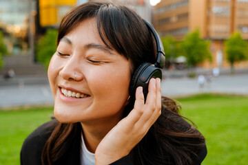 Young asian woman in headphones listening music while sitting on grass