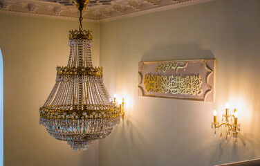 A large beautiful chandelier hangs on the ceiling against the background of inscriptions and lamps...