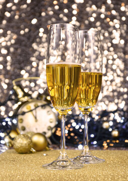Two glasses of champagne at New Year's Eve party golden shiny background stock images. Glasses champagne against holiday lights vertical photo. New Year party still life with champagne and clock image