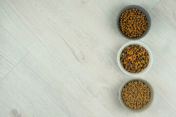 Diversity of dry fodder for cats and dogs in ceramic bowls on a white wooden background. Top view. Copy space.