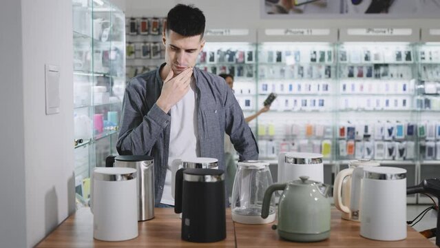 A man in an electronics store chooses an electric kettle with Wi-Fi and automatic functions.