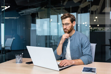 .Serious pensive businessman in shirt thinking about decision sitting at table in modern office,...