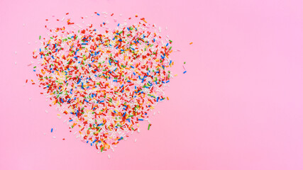 Bunte Zuckerstreusel in Herz-Form auf einem rosa Hintergrund von oben