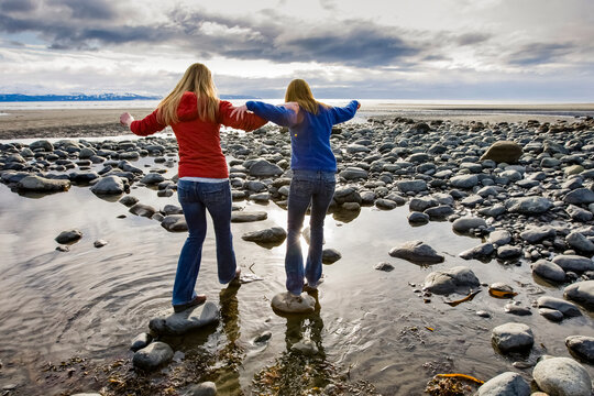 Two Young Women Walk Across Rocks At Bishop's Beach In Homer, Alaska