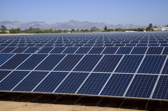 Close-up of solar panels with farm buildings and mountains beyond, near Blythe; California, United States of America