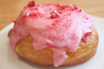 Closeup of Mouthwatering strawberry-glazed with raspberry cream filling doughnut 