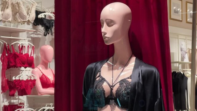 Female mannequin in black lace lingerie and a black silk peignoir stands in the window of a lingerie store