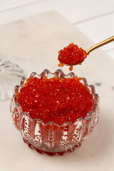 A man's hand holds a spoonful of red caviar over a glass bowl