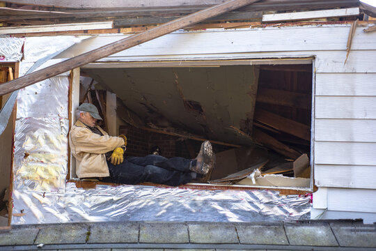 Man snoozing on a worksite, sitting on the ledge of an open window under repair; Olympia, Washington, United States of America