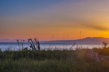 The setting sun over Alaska's Mount Susitna, locally known as 'The Sleeping Lady', with the Cook Inlet in the foreground as seen from Point Worzenoff Beach; Anchorage, Alaska, United States of America