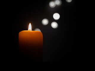 Orange colored candle burning in the dark and bokeh lights on a black background with empty space...