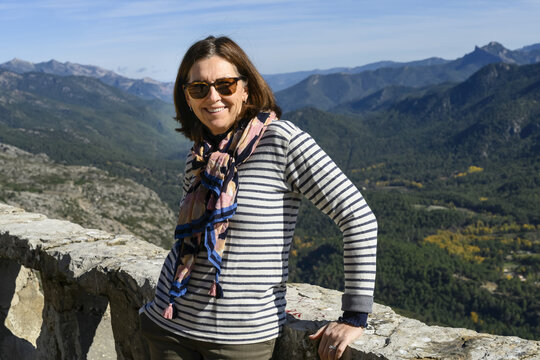A mature woman stands smiling for the camera with the Sierra de Cazorla mountain range in the background; Cazorla, Jaen Province, Spain