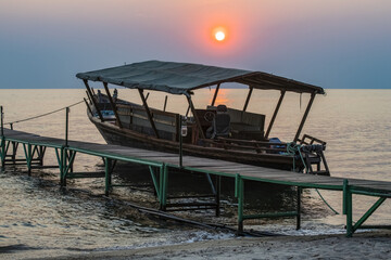 Sun setting behind boat moored to dock at Mbali Mbali Mahale Lodge (Kungue Beach Lodge) on Lake Tanganyika; Tanzania