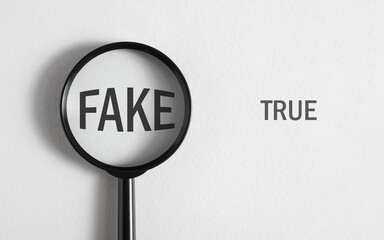 Concept of choosing between true and fake. Magnifying glass focused on word Fake on white...