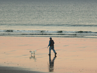 Fototapeta na wymiar Man walking dog on leash at beach