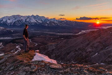 A hiker observes sunset from a mountain ridge in the Alaska Range; Alaska, United States of America