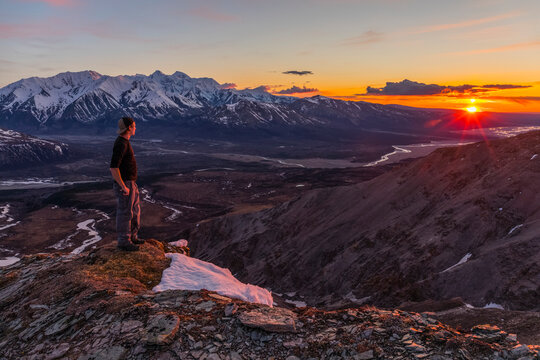 A hiker observes sunset from a mountain ridge in the Alaska Range; Alaska, United States of America