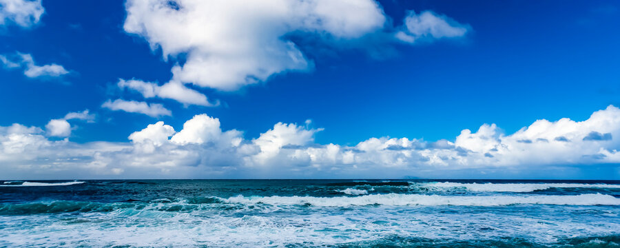 Ocean surf rolls into shore with the horizon meeting cloud and blue sky; Honolulu, Oahu, Hawaii, United States of America