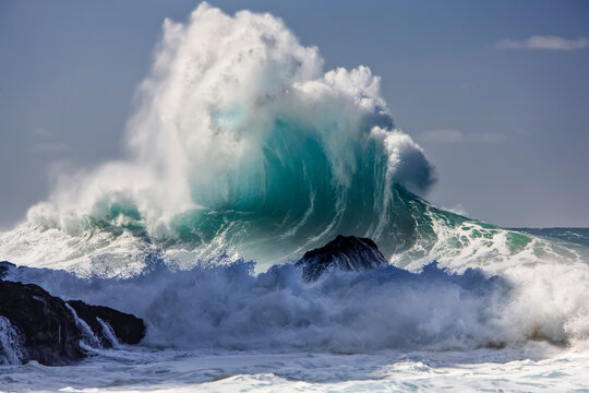 Large ocean wave crashes into rock along the coastline of a Hawaiian island; Hawaii, United States of America