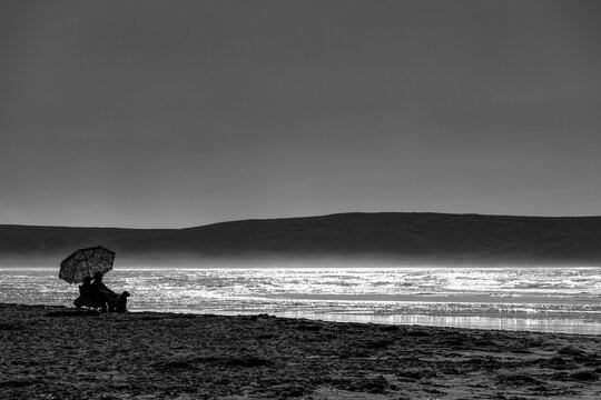 Black and white image of a couple sitting on Dillon Beach at the water's edge looking out to the ocean; California, United States of America