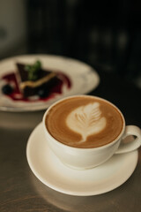 Photo of tasty cheesecake with cup of cappuccino in focus. Cup of coffee standing on silver table near plate with dessert.