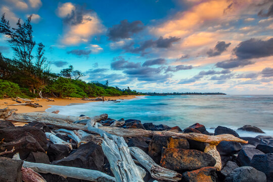 Sunrise over Lydgate beach and ocean with rocks and driftwood in the foreground and the coastline in the distance; Kapaa, Kauai, Hawaii, United States of America