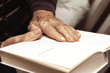 An elderly man, a grandfather, holds an open book in his hands. Leisure for the elderly. Reading a...