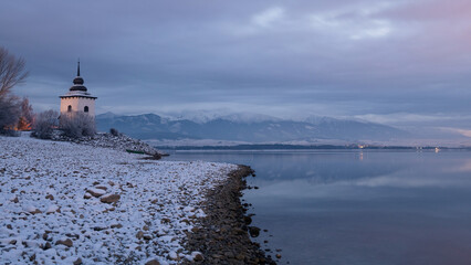 Fototapeta premium Church Tower of Virgin Mary at the shore of The Liptovska Mara dam in the morning light at winter, the area of Liptov in Slovakia
