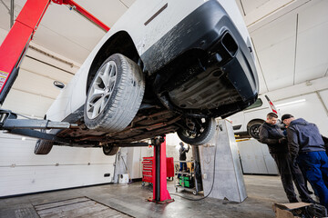 Two mechanic in service repair station working with muscle car in lift.